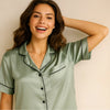 Woman wearing light green silk pajamas with black piping, smiling and posing against a plain background.