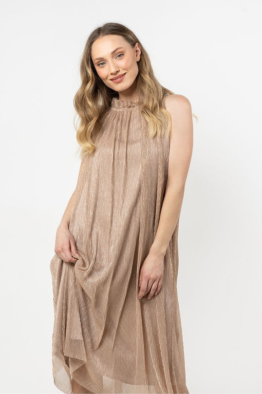 Smiling female model wearing a sleeveless rose gold metallic pleated midi dress with a high neckline gently holding the skirt against a white background