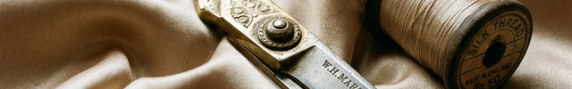 A pair of elegant, antique gold heavy tailor's scissors resting on draped, liquid-like champagne silk satin fabric.