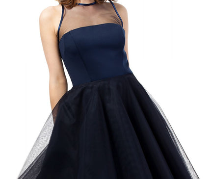 A female model in a navy blue satin bodice and tulle A-line sleeveless dress with a sheer mesh yoke stands facing the camera against a plain white background