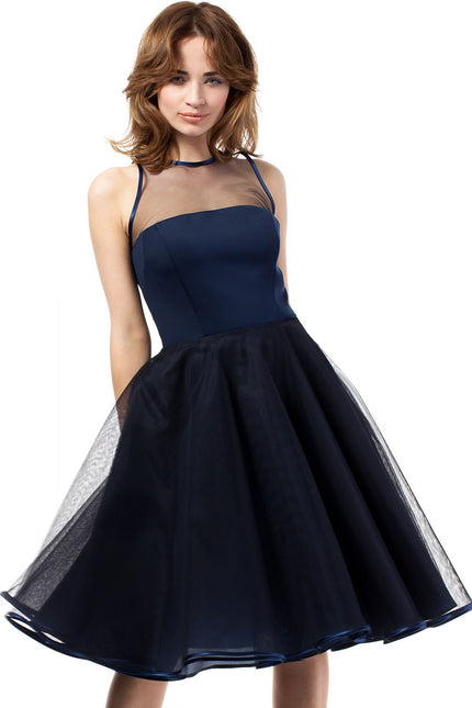 A female model in a navy blue satin bodice and tulle A-line sleeveless dress with a sheer mesh yoke stands facing the camera against a plain white background