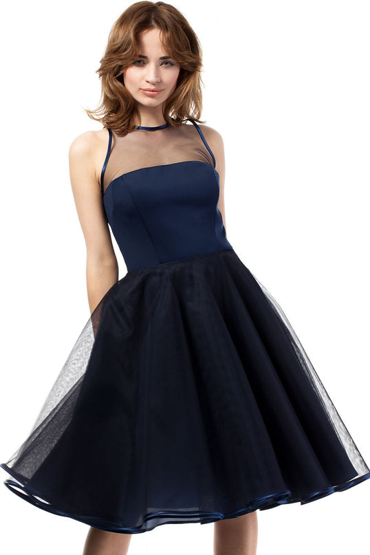 A female model in a navy blue satin bodice and tulle A-line sleeveless dress with a sheer mesh yoke stands facing the camera against a plain white background