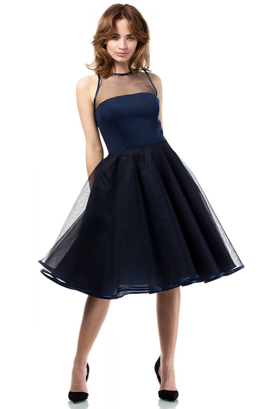Female model in a navy blue spaghetti strap mesh yoke fit and flare tulle midi dress standing with legs apart against a plain white background