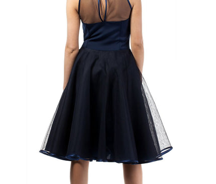 Female model standing with her back to the camera against a white backdrop in a navy satin and sheer mesh cocktail dress with a full flared organza skirt