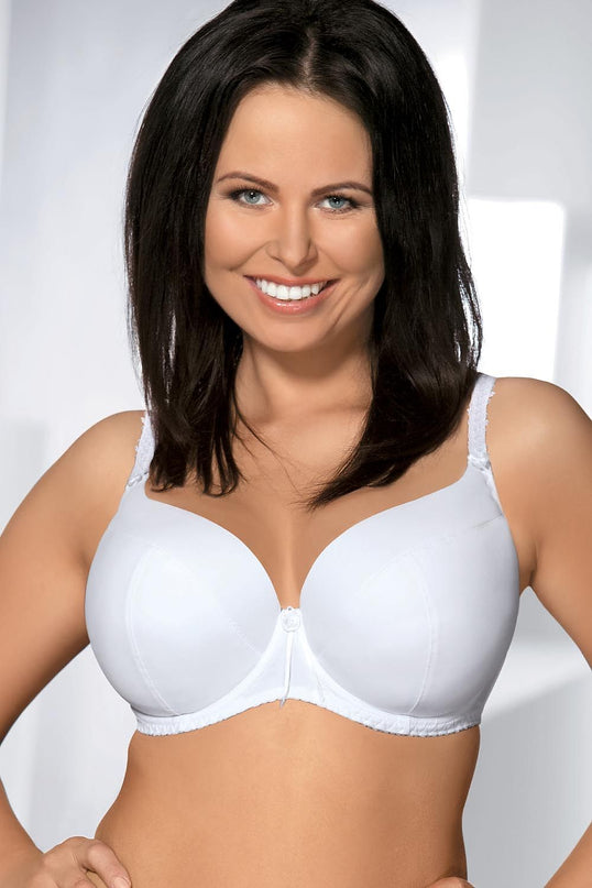 A smiling model stands facing the camera wearing a white smooth moulded underwired bra with lace-trimmed straps against a white wall background