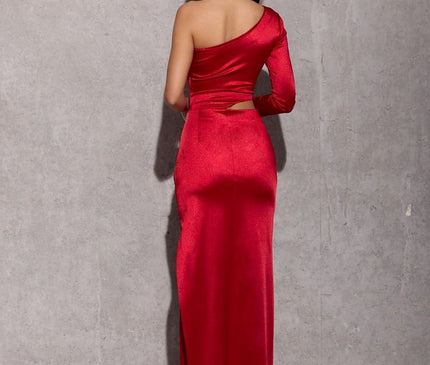 A model stands with her back to the camera wearing a red satin one-shoulder full-length fitted evening gown against a concrete wall and floor