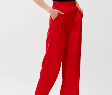 Model wearing high-waisted wide-leg red satin trousers and a fitted black short-sleeve top standing with hands in pockets against a white studio background
