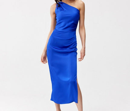 Female model standing on a white studio floor wears a cobalt blue satin one-shoulder midi dress with a side slit