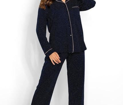 Model wearing a navy cotton polka dot long-sleeve button-up pyjama top with piped trim and matching straight-leg trousers stands barefoot against a white background