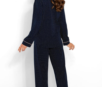 A female model stands barefoot against a white backdrop wearing a navy blue cotton polka dot pyjama set with straight-leg trousers and long sleeves while looking over her shoulder