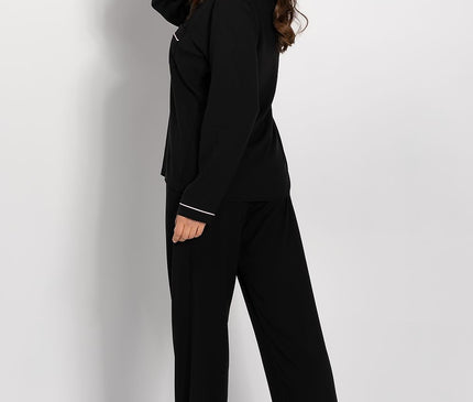 Female model wearing a black jersey long-sleeve button-front pyjama top and wide-leg bottoms in a side pose barefoot against a plain white studio background