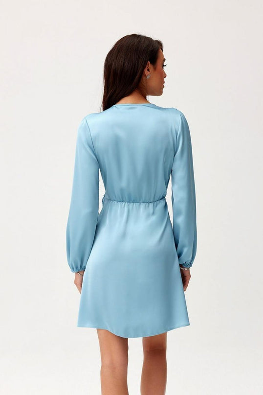 Female model standing back to camera wearing a light blue satin long sleeve mini dress with cinched waist against a plain white background
