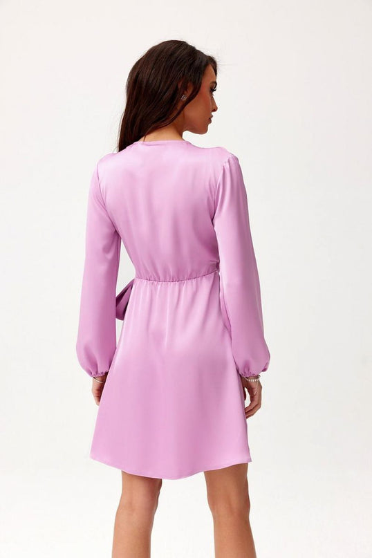 Woman model seen from the back with head in profile wearing a lilac satin long-sleeved A-line mini dress with cinched waist against a plain white background