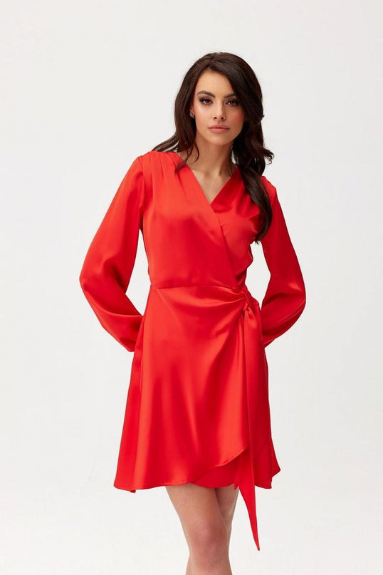 A female model stands against a white background wearing a red satin wrap mini dress with a V-neckline, long sleeves and a tied waist