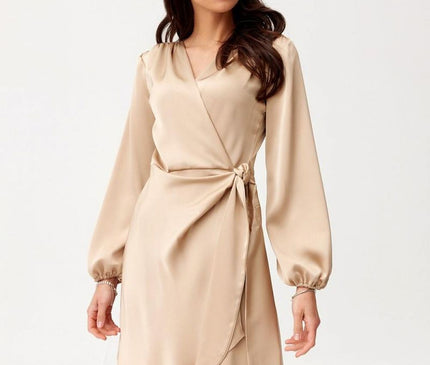 Female model wearing a beige satin wrap mini dress with long bishop sleeves stands against a plain white studio background looking to the side