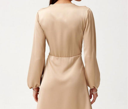 A female model stands with her back to the camera wearing a beige satin long sleeve mini dress with a flared cut against a plain white background