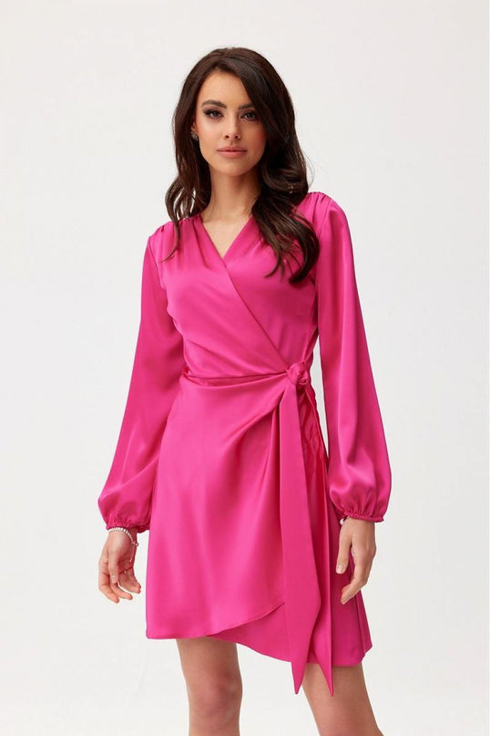 Model wearing a fuchsia satin wrap mini dress with long bishop sleeves standing against a white background