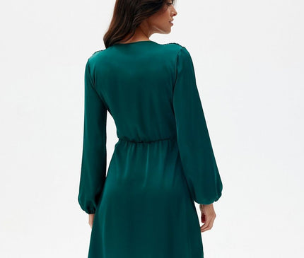 Female model wearing a teal green long-sleeve satin mini dress with an elasticated waist standing with her back to the camera and head turned to the side against a plain white backdrop
