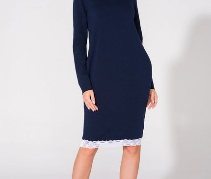 Female model wearing a navy blue knit long sleeve straight cut midi dress with white lace trim at the hem standing against a plain white studio backdrop