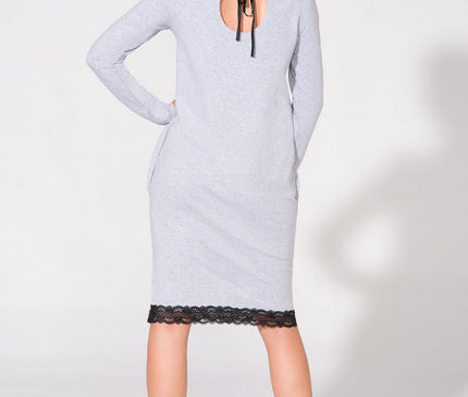 Female model standing in back view wearing a light grey long-sleeve jersey midi dress with black lace hem and a back keyhole tie on a plain white background