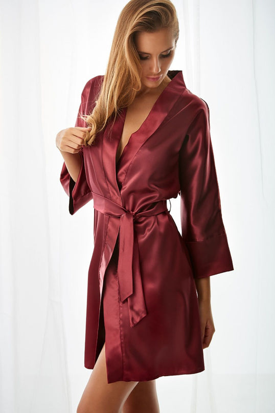 Female model wearing a burgundy satin belted kimono-style robe with three-quarter sleeves and mid-thigh cut gently touching her hair as she stands in front of sheer white curtains