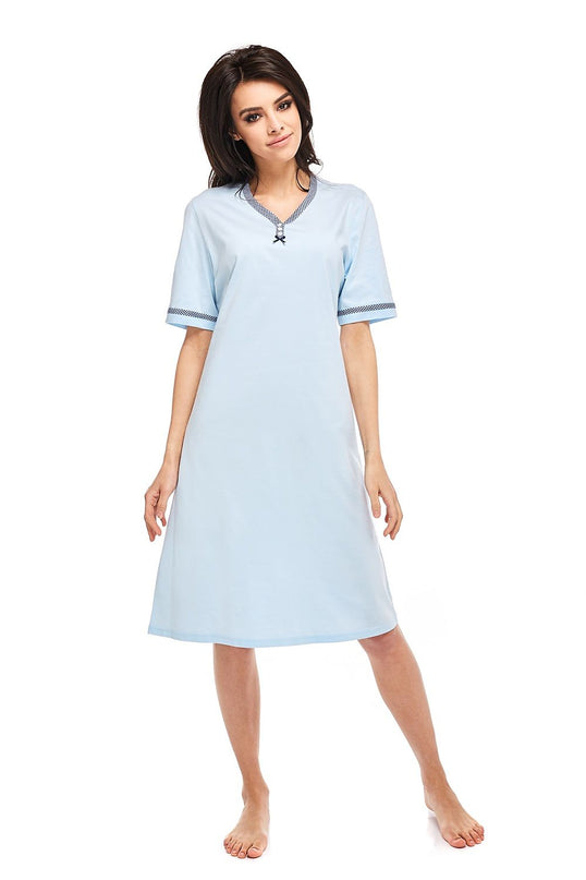 Female model wearing a light blue cotton A-line nightdress with short sleeves and gingham trim at the V-neck and cuffs standing barefoot against a plain white background