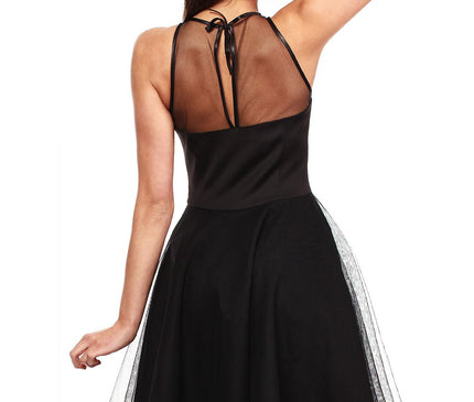 A model stands against a white background wearing a black sleeveless satin dress with sheer mesh yoke and tulle overlay A-line skirt shown from the back with one arm raised over her head
