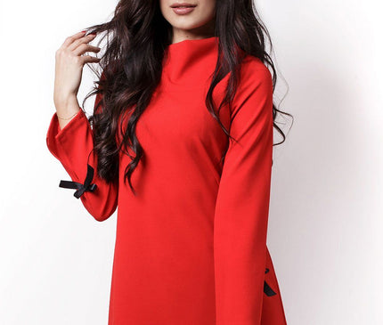 Female model standing against a white background wearing a red long-sleeve jersey A-line shift dress with black bow details