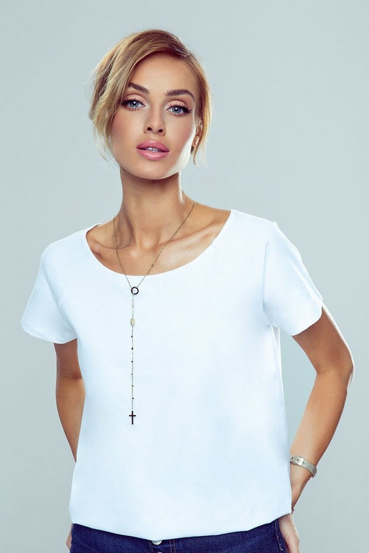A model stands against a light grey backdrop with her hands in her pockets wearing a loose-cut white cotton T-shirt with short sleeves and a round neckline