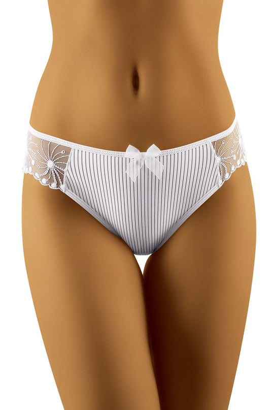 Female model wearing white ribbed fabric bikini-cut briefs with floral lace side panels and bow detail standing against a plain white background