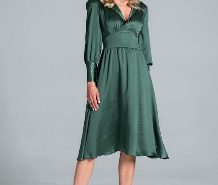 Female model standing against a pale grey studio backdrop wearing an emerald green satin midi dress with a wrap bodice long sleeves and flared skirt