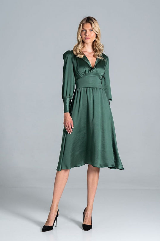 Female model standing against a pale grey studio backdrop wearing an emerald green satin midi dress with a wrap bodice long sleeves and flared skirt