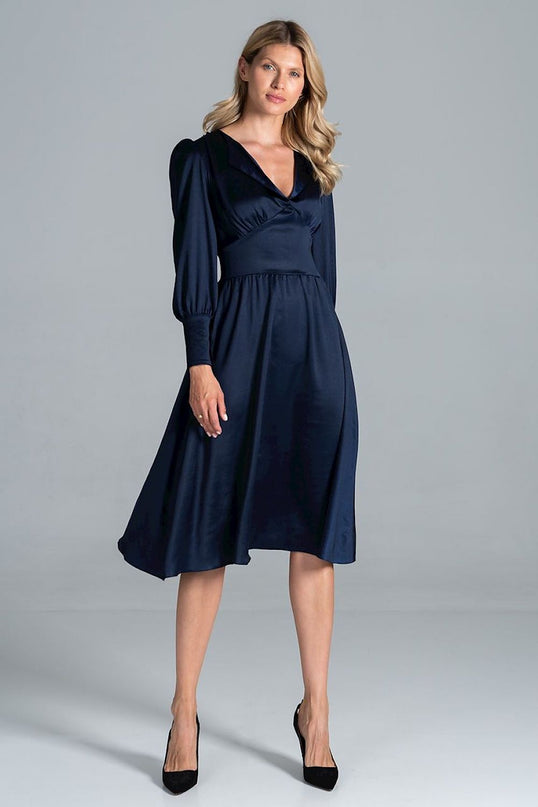 Female model standing against a plain light grey background wearing a navy satin V-neck long-sleeve midi dress with a fitted waist and flared skirt