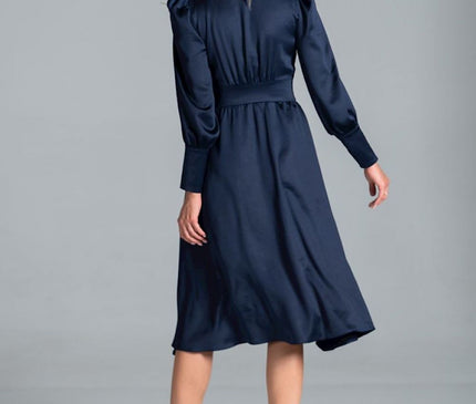 Female model in a navy satin long-sleeve midi dress with puffed shoulders and flared skirt standing back to camera against a plain grey studio background
