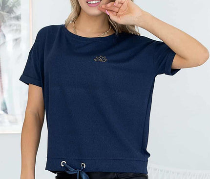 Female model standing against a white wall with framed artwork wearing a relaxed-cut navy jersey short-sleeve top with drawstring hem and a black faux leather mini skirt while holding a gold clutch