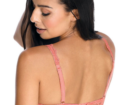 A female model wearing a coral pink lace bra with adjustable straps and scalloped edges posed looking over her shoulder against a white background