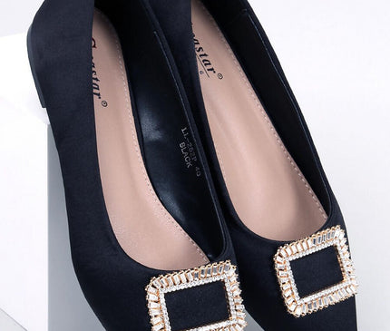 Black satin pointed-toe flat shoes topped with a crystal-embellished square buckle angled on a white block against a plain white background