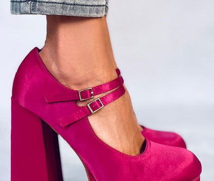 Model’s foot in cropped denim jeans wearing fuchsia velvet Mary Jane platform heels with double buckle straps and chunky block heel standing on a pale grey studio floor