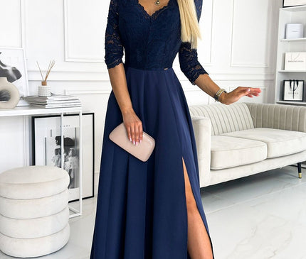 Female model holding a nude clutch wearing a navy blue lace bodice and flowing chiffon maxi dress with three-quarter sleeves and high side slit in a bright room with white panelled walls cream sofa marble floor and minimalist decor