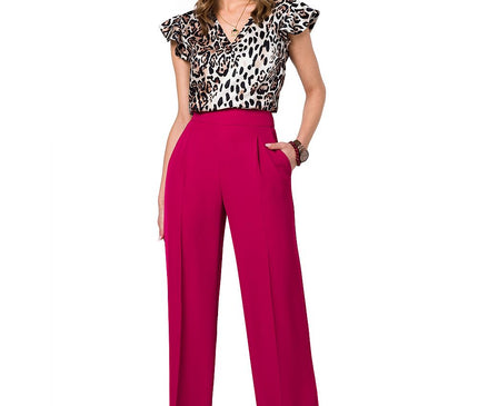 Model wearing a silky leopard-print V-neck blouse with flutter sleeves paired with magenta high-waisted wide-leg trousers standing with one hand in pocket against a white background