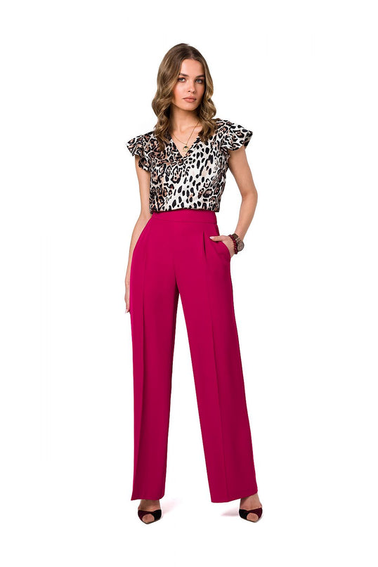 Model wearing a silky leopard-print V-neck blouse with flutter sleeves paired with magenta high-waisted wide-leg trousers standing with one hand in pocket against a white background