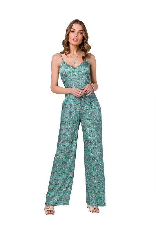 A female model stands front-on against a white background wearing a green patterned satin jumpsuit with spaghetti straps, a V-neckline and wide-leg cut with her hands clasped at her waist