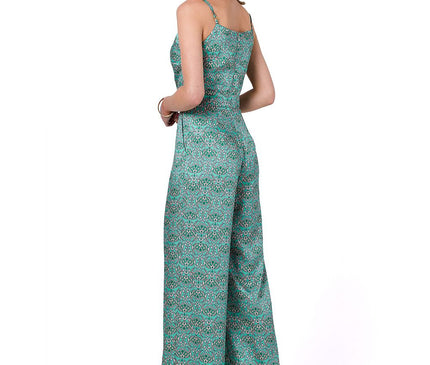 Model in a green printed spaghetti strap wide-leg jumpsuit standing in a three-quarter back pose against a white studio background