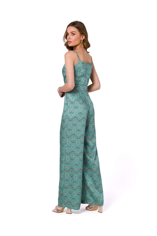 Model in a green printed spaghetti strap wide-leg jumpsuit standing in a three-quarter back pose against a white studio background