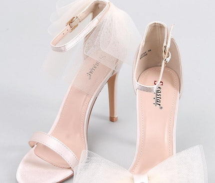 A pair of blush pink satin open-toe stiletto sandals with thin ankle straps and tulle bows displayed on a light grey background