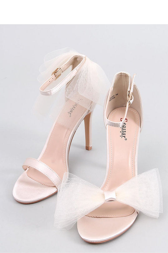A pair of blush pink satin open-toe stiletto sandals with thin ankle straps and tulle bows displayed on a light grey background