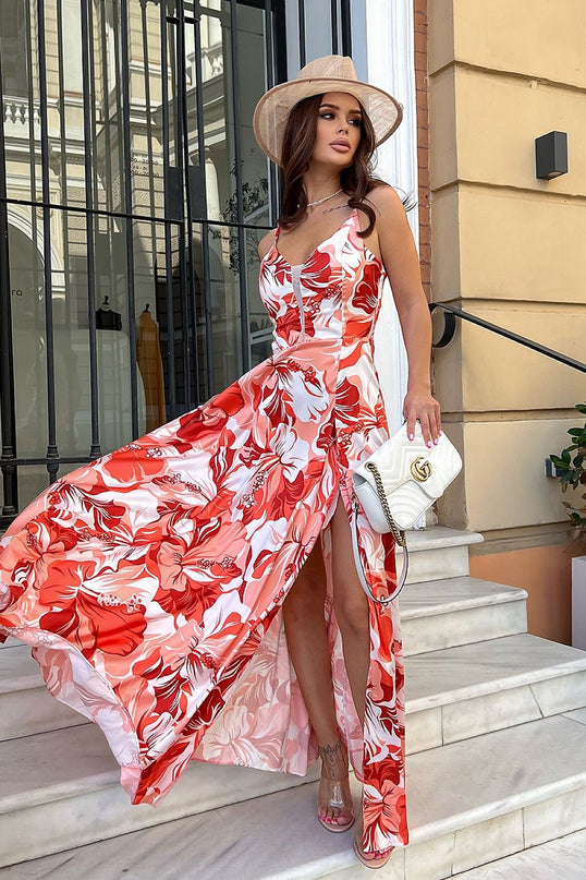 Female model standing on white marble steps in front of a wrought iron gate and cream building facade wearing a red and white floral satin maxi dress with spaghetti straps and thigh-high slit