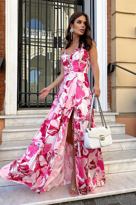 female model wearing a sleeveless satin maxi dress with a fitted bodice and flared skirt with front slit in pink and white abstract print standing on marble steps in front of a wrought iron gate and stone building facade