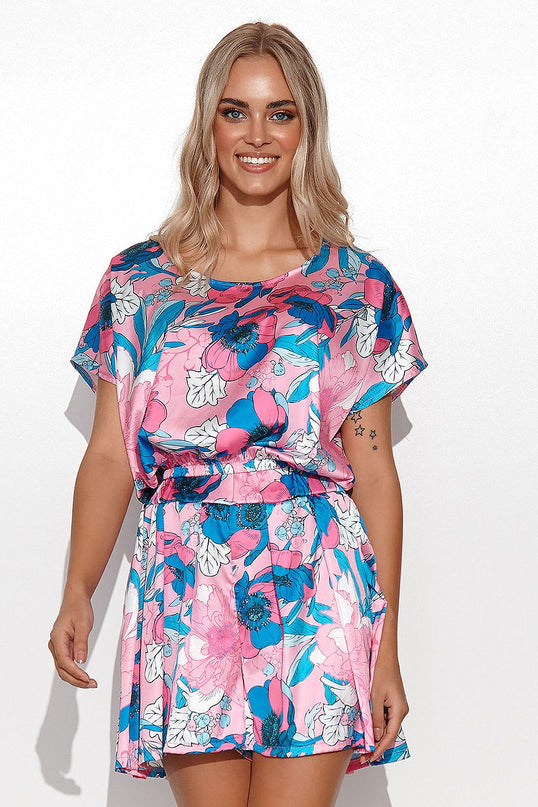 A smiling model stands front on wearing a pink satin short-sleeve elastic-waist floral mini dress with a flared skirt against a plain white wall background