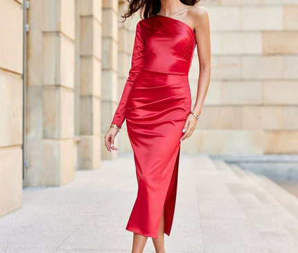 Female model walking forward in a red satin one-shoulder midi dress with a side slit against a pale stone columned facade background